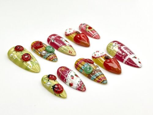 Strawberry press-on nails from the side, with olive ladybug nails, plaid pink tips and a glossy red strawberry nail