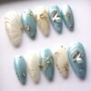 Icy blue and pearl white almond press-on nails laid flat, with gold starbursts, wire bows and a teardrop crystal