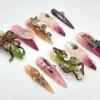 Sculpted garden press-on nails scattered on white: a 3D butterfly with leaf wings, pink-to-plum fades and tiny gems