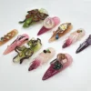 Another view of the stiletto press-on nails: an olive-green leaf butterfly, a pearly oval and amber, pink and plum tones