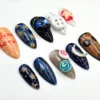 Peach, navy and brown press-on nails flat on white, with orange welcome home lettering, a swirl candy, a moon and a button