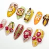 Fruit press-on nails from the other side: a strawberry-hat cat, cherry cat faces, banana toast and a golden banana nail