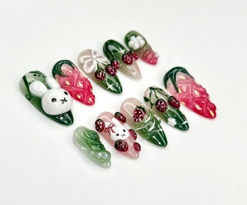 Jade green and pink press-on nails flat on white, with sculpted white bunny faces, red strawberries and lattice pink nails