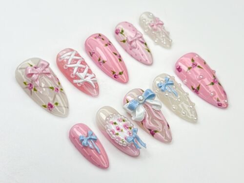 Sheer pink almond press-on nails flat on white, with tiny rosebud paintings, blue and pink 3D bows and white corset lacing