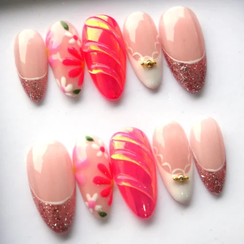 Close angle of almond French-tip press-on nails: a ridged neon pink nail, glitter tips and a white nail with a gold bead