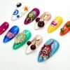 Higher angle of the pop art press-on nails, with a red fish on blue, a pearl-framed green jewel and glossy cherries