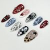 Mismatched almond press-on nails flat on grey: red spirals, plaid, leopard print, blue line-drawn faces and rhinestones