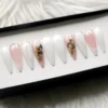 Pearl white press-on nails seen from the other end of the tray, with shell chips, gold foil and pink tips