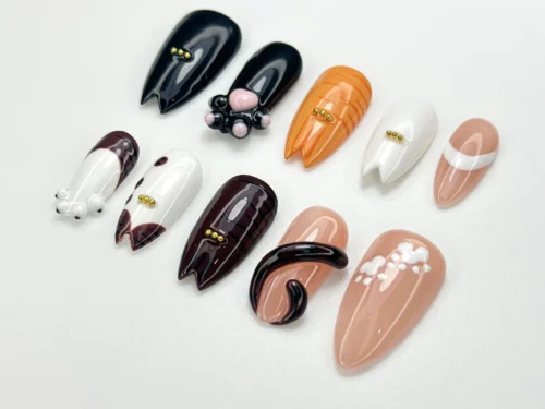 Angled view of cat press-on nails showing a curled black tail, a pink paw pad and ear-shaped tips on tabby nails