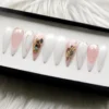 Ten stiletto press-on nails on a white tray: milky white, pink French tips, silver lines and shell chips