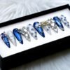 Navy chrome and pale grey stiletto press-on nails on a black display box with silver gems, chain trim and a butterfly