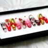 Cherry press-on nails from the opposite angle in a black box, showing red crystals, a jewelled heart and gold chrome