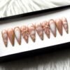 Mirrored view of caramel and cream marbled press-on nails, showing gold foil edging and two raised nude flowers