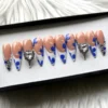 Blue flower French tip press-on nails in a black-edged tray, with rhinestone-edged heart crystal accent nails