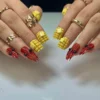 Two hands wearing corn-cob and crawfish press-on nails against a white surface, with gold rings and red pointed claws