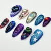 Cosmic press-on nails from another angle: a blue nail covered in white stars, a green gem cluster and purple spiral nails