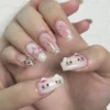 Milky pink coffin press-on nails on fingers with 3D kitty-face charms, a pink star nail, pearl chains and leopard tips