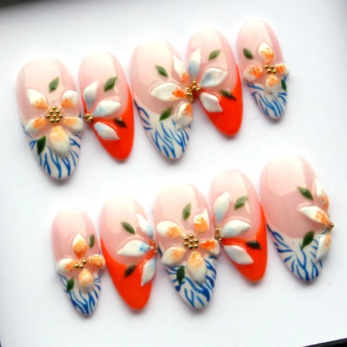 Almond press-on nails with sculpted white and orange petals, blue zebra-line tips and gold centres, laid flat