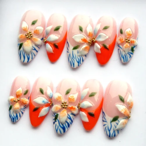 Floral press-on nails flat on white: tangerine French tips, 3D petals, green leaves and blue wavy-line tips