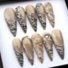 Angled view of sheer champagne press-on nails with silver chrome vine and net details, clear water-drop domes and gems