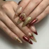 Burgundy and gold press-on nails worn on two hands, with a gem in a gold frame, tiny gold roses and a red chrome tip