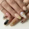 Close view of cat press-on nails on a hand with silver rings: a black cat, a calico cat face and a gold swirl nail