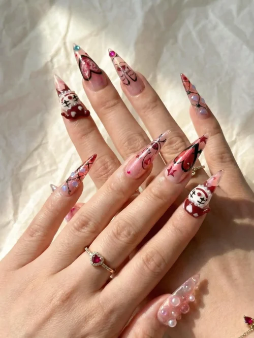 Stiletto press-on nails worn on a hand with a ring: pink tips, jester faces, checks and 3D pearl beads