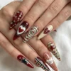Worn on two hands: red and cream stiletto press-on nails with a heart, a swirl, gingham, rhinestones and stars