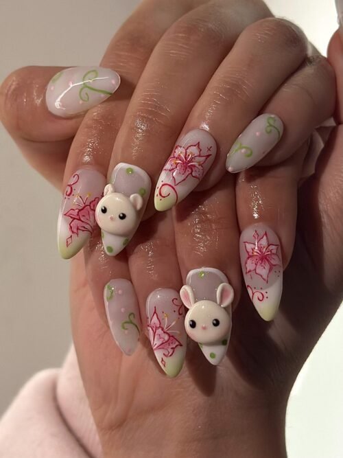 Milky pale press-on nails worn on a hand, with pink lilies, green vines and two cream sculpted mouse faces