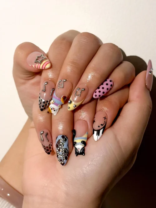 Press-on nails worn on a hand: nude and pink polka dot nails, black-and-white cat designs and silver music-note details