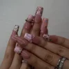 Blush pink long square press-on nails worn on both hands, showing white bows, leopard tips and a gold band