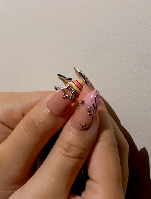 Close-up of two long press-on nails held up: a nude nail with a silver star charm and a pink nail with a glitter swirl