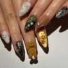 Press-on nails worn on a hand with a fuzzy brown teddy bear, a bee on yellow, olive green and chrome nails, and pearls