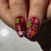 Close-up of two press-on nails in burgundy plaid, with green star-shaped buttons, a white button and small black stars
