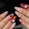 Plaid and polka-dot press-on nails worn on a hand, with red outline stars, stitched apple halves and tiny orange bear charms