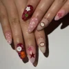 Pink polka-dot and burgundy plaid press-on nails worn on a hand, with red star outlines, stitched apples and a white button