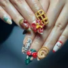 Cottagecore press-on nails worn on a hand: a yellow waffle with a red bow, cinnamon roll, red mushrooms and an apple half