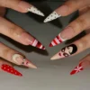 Stiletto press-on nails on a hand in another pose: polka-dot white tips, striped red tips and a painted face with a dark bob
