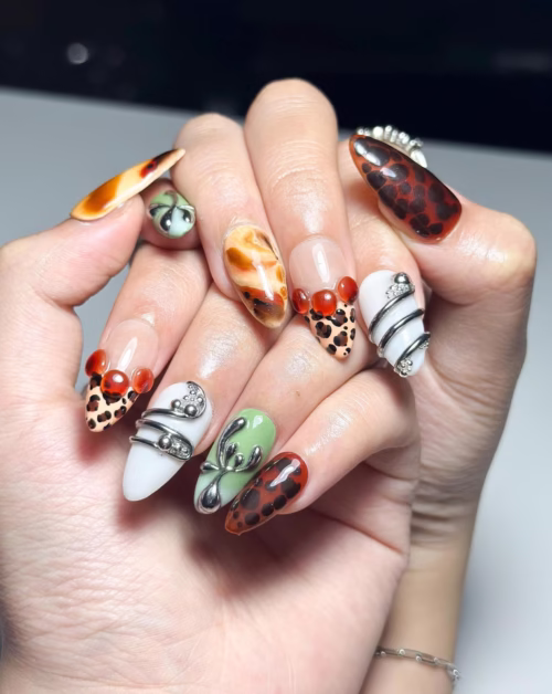 Tortoiseshell, moss green and leopard-tip almond press-on nails worn on a hand with chrome coils and red cherries