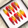 Angled view of red-to-gold ombré press-on nails, with silver chrome swirls on the red accent nails