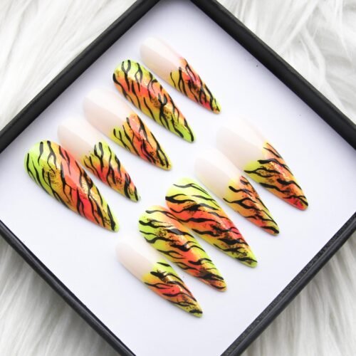 Angled view in the box on white fur: neon lime-to-orange tiger-stripe press-on nails with sheer nude cuticle ends