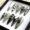 Angled view of gunmetal press-on nails with black and white spots, a 3D bow nail and small chrome beads