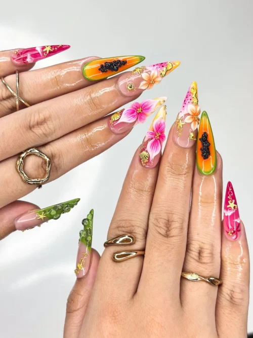 Worn on two hands with gold rings: stiletto press-on nails with papaya halves, pink hibiscus and green bubble tips