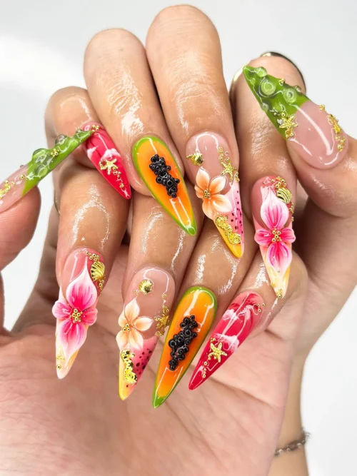 Stiletto press-on nails worn on a hand with a painted papaya, 3D hibiscus, green bubble tips and gold starfish