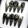 All ten black and gunmetal stiletto press-on nails laid out on white, with raised silver ridges, a heart shape and studs
