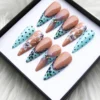 Aqua polka dot and nude French tip press-on nails in a box on white fur, with navy lace edges and white flowers