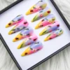 Pink, lilac and yellow press-on nails angled in a black box, hand-painted with bees, ladybugs, leaves and daisies