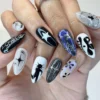 Black, white and grey almond press-on nails worn on a hand, with star shapes, hand-lettered text and a spider-web nail