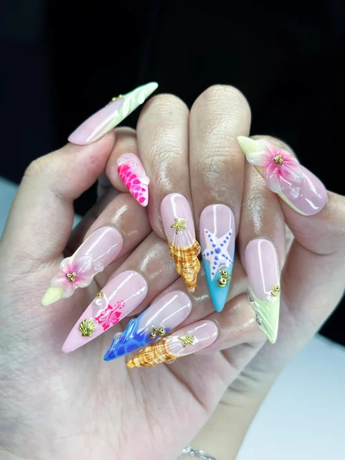 Pink stiletto press-on nails worn on a hand: green, orange and blue shell tips, a blue starfish and 3D hibiscus
