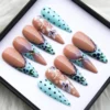 Stiletto press-on nails in aqua dots and nude with navy lace tips, painted blueberries and a gem, box on fur